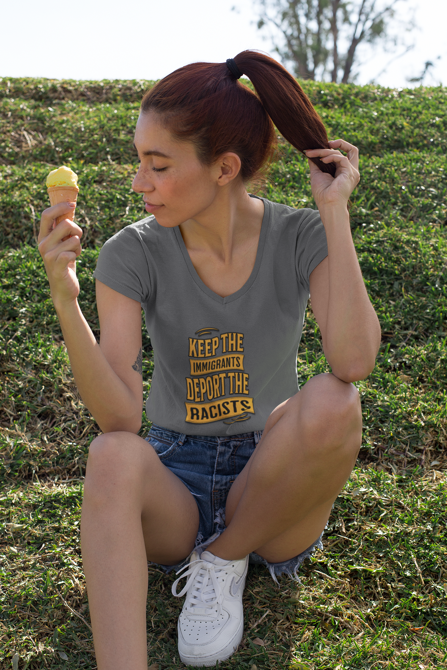 Woman sitting on grass wearing a t-shirt with a political message, holding an ice cream.